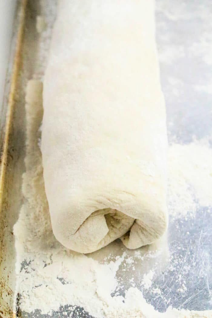 Rolled Philly Cheesesteak Stromboli dough log on a floured metal baking sheet, ready for baking.