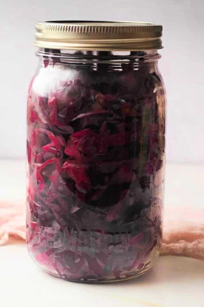 A jar of purple pickled cabbage with a metal lid rests on a light surface, showcasing the vibrant color and tangy aroma reminiscent of a classic pickled red cabbage recipe.