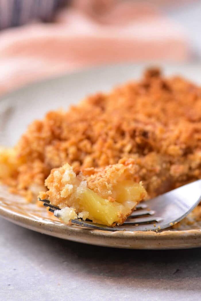 Close-up of a fork with a bite of pineapple crumble on a plate, evoking memories of a pineapple casserole recipe, showcasing its crumbly topping and soft filling.
