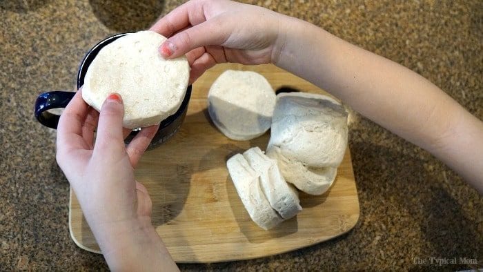 Hands holding biscuit dough over a cutting board with more dough pieces—imagine the same simplicity applied to creating pizza in a mug, transforming basic ingredients into something delightfully unexpected and easy.
