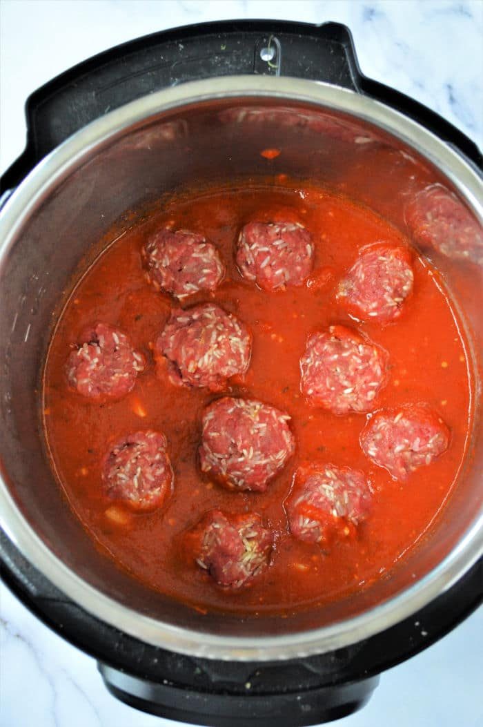An instant pot filled with raw porcupine meatballs nestled in a rich red tomato sauce, ready for cooking. The cooker sits elegantly on a marble countertop.