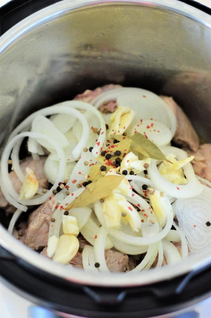 Sliced onions, garlic, bay leaves, and peppercorns on top of meat in this easy pork adobo Instant Pot recipe.