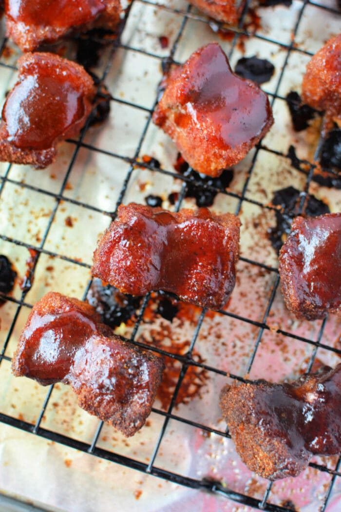 Crispy glazed pork belly burnt ends cooling on a wire rack over a foil-lined baking sheet—a mouthwatering recipe in the making.