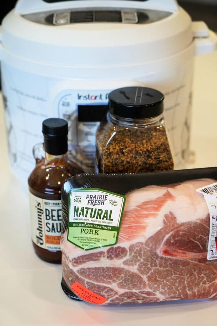 Pork butt nestled in the Instant Pot, accompanied by a bottle of beef sauce and a jar of spices, creates an enticing aroma on the countertop.