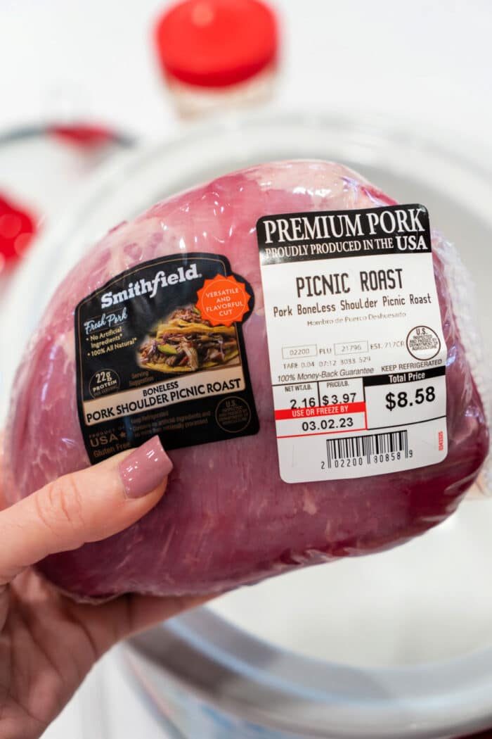 A hand holds a packaged Pork Picnic Roast, its label clearly displaying the price and weight.