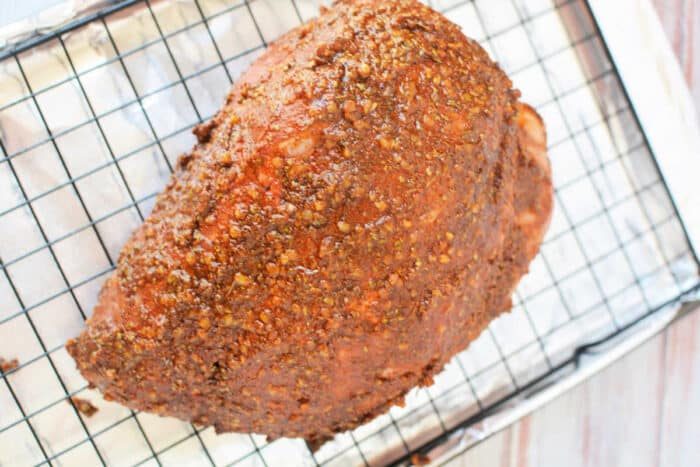 Seasoned ham on a wire rack over a foil-lined baking sheet, prepared like a classic pork roast recipe, ready for the oven.