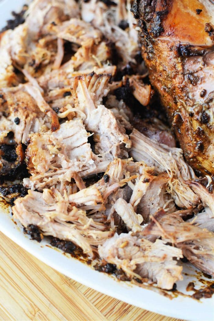 Shredded, seasoned pork roast on a white plate atop a wooden surface—solid for showing off your favorite oven pork roast recipe.