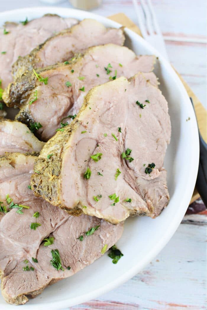 Slices of seasoned tender pork roast, are garnished with fresh parsley on a white plate, achieving results rivaling the Instant Pot's efficiency.