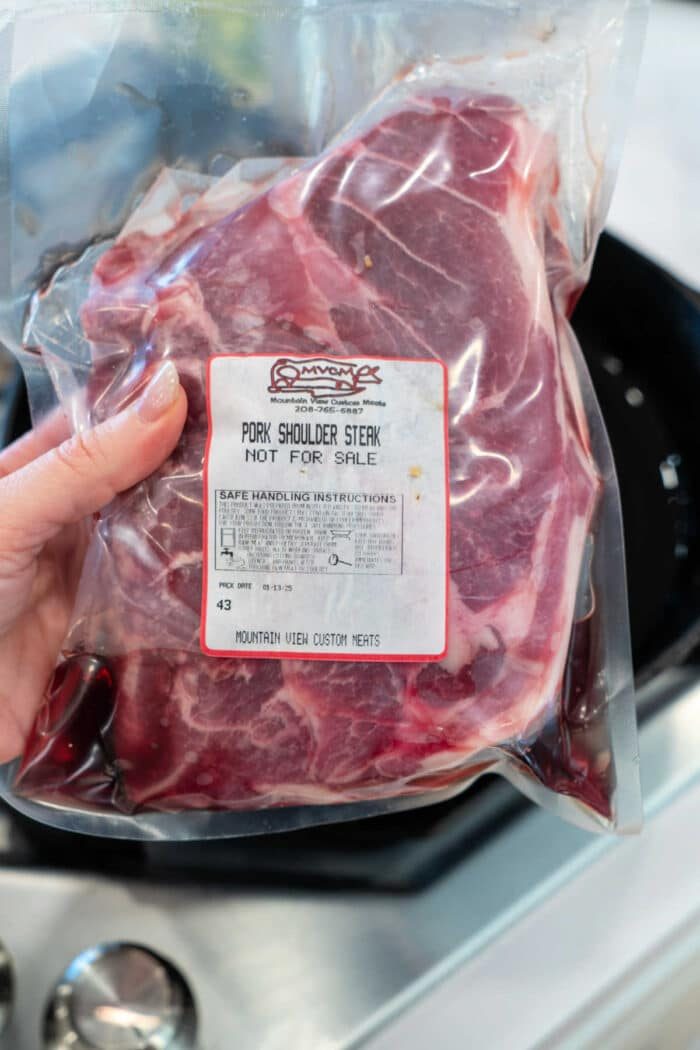 A hand holds a vacuum-sealed package of Pork Shoulder Steak labeled Not For Sale.
