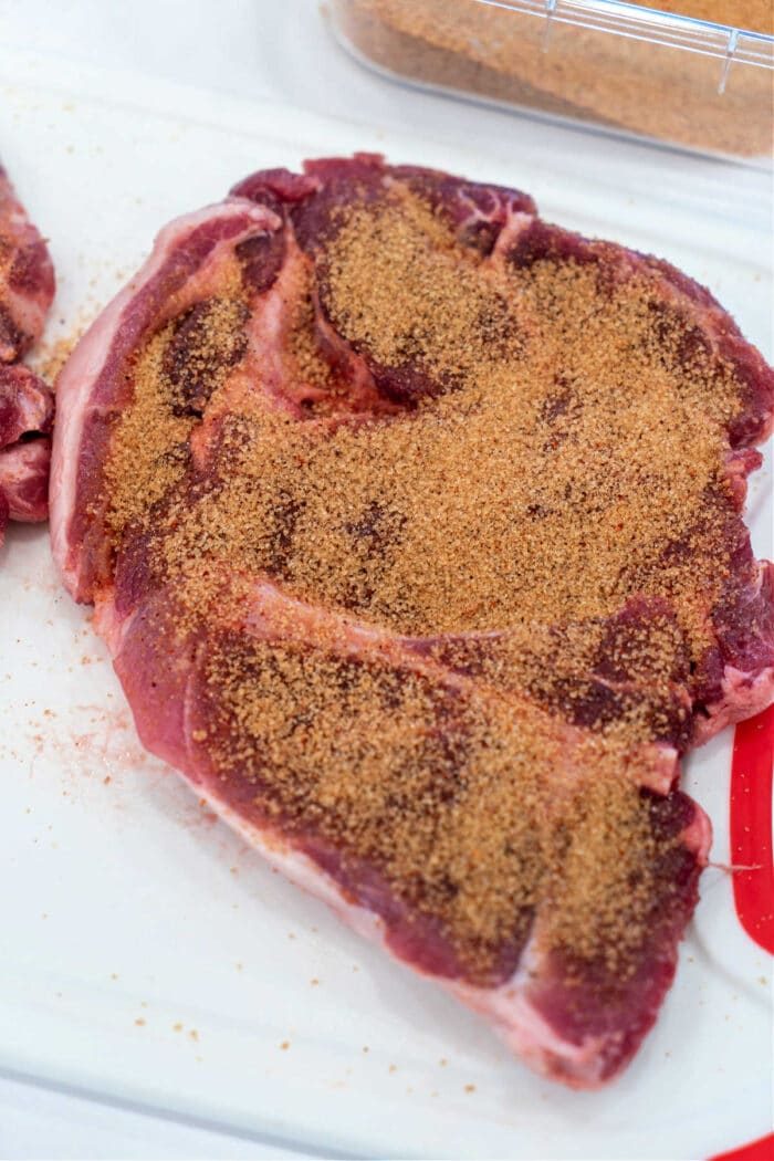 Pork shoulder steak on a cutting board sprinkled with a layer of dry seasoning rub.