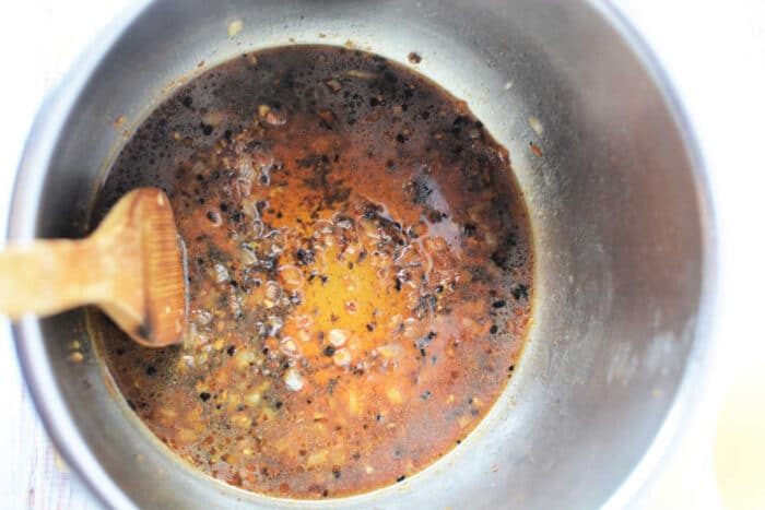 A pressure cooker pot with a wooden spoon, filled with a simmering dark brown, oily sauce with seasonings—solid for enhancing your favorite Pork Steak Recipe.