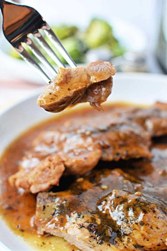 A fork holds a bite of tender meat above a plate of saucy, seasoned pork steak, showcasing a mouthwatering pork steak recipe.