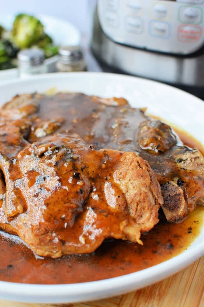 Plate of tender pork steaks covered in brown gravy, featuring a good Pork Steak Recipe. An Instant Pot and broccoli are visible in the background, hinting at a wholesome homemade Pork Steak meal.
