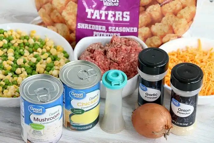 Ingredients for a potato tot casserole with ground beef: tater tots, mixed veggies, cheese, onion, soup cans, and seasonings.