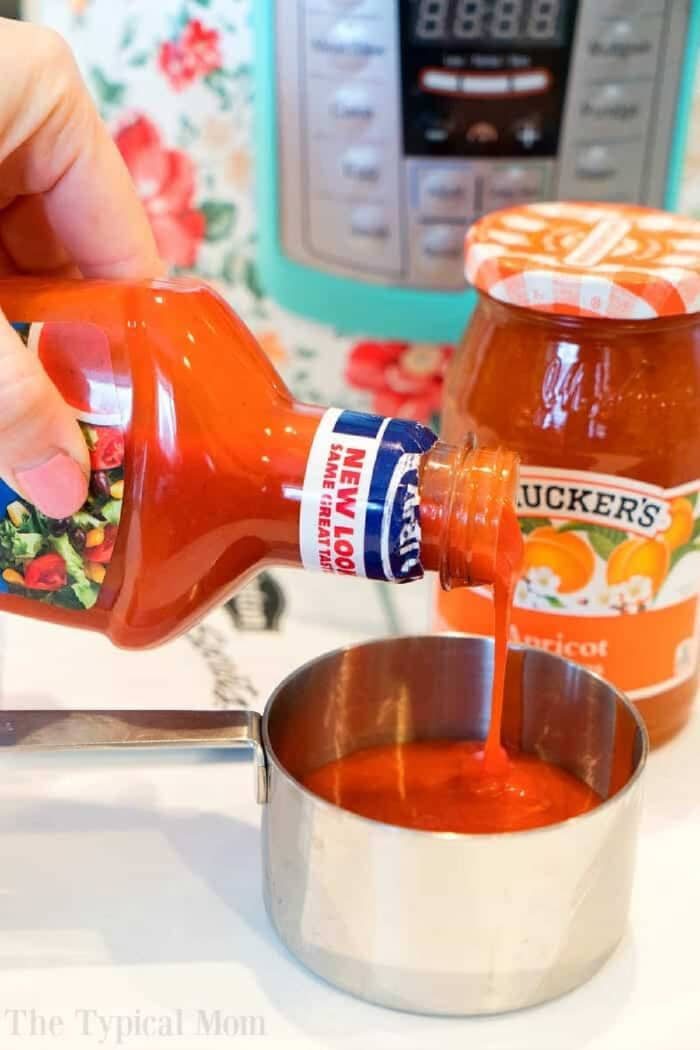 Hand pouring catalina dressing into a measuring cup, with a jar of apricot preserves in the background—solid ingredients for pressure cooker apricot chicken.