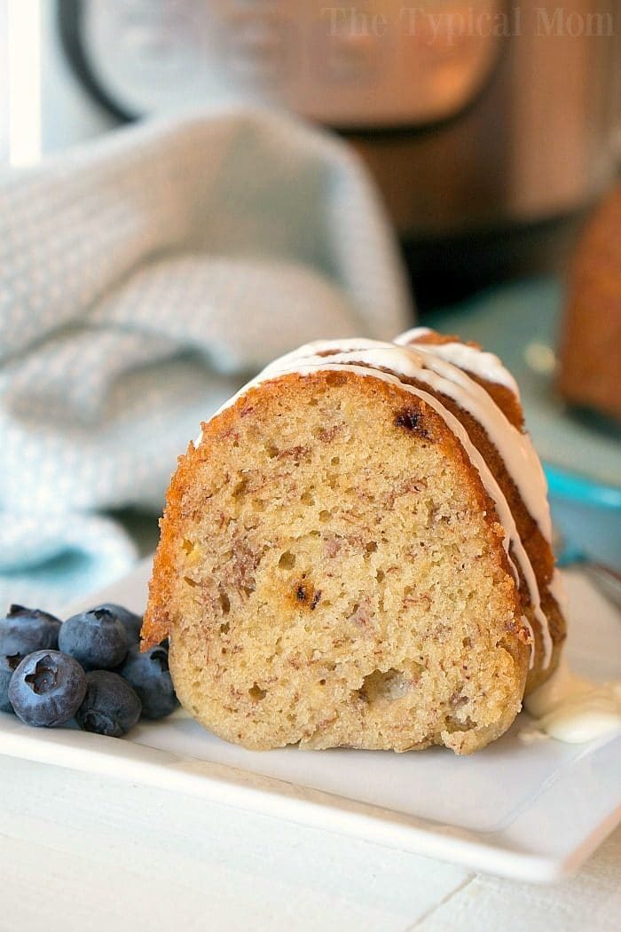 A slice of banana bread in a mini bundt cake with icing drizzled on top cooked in pressure cooker served alongside fresh blueberries on a white plate