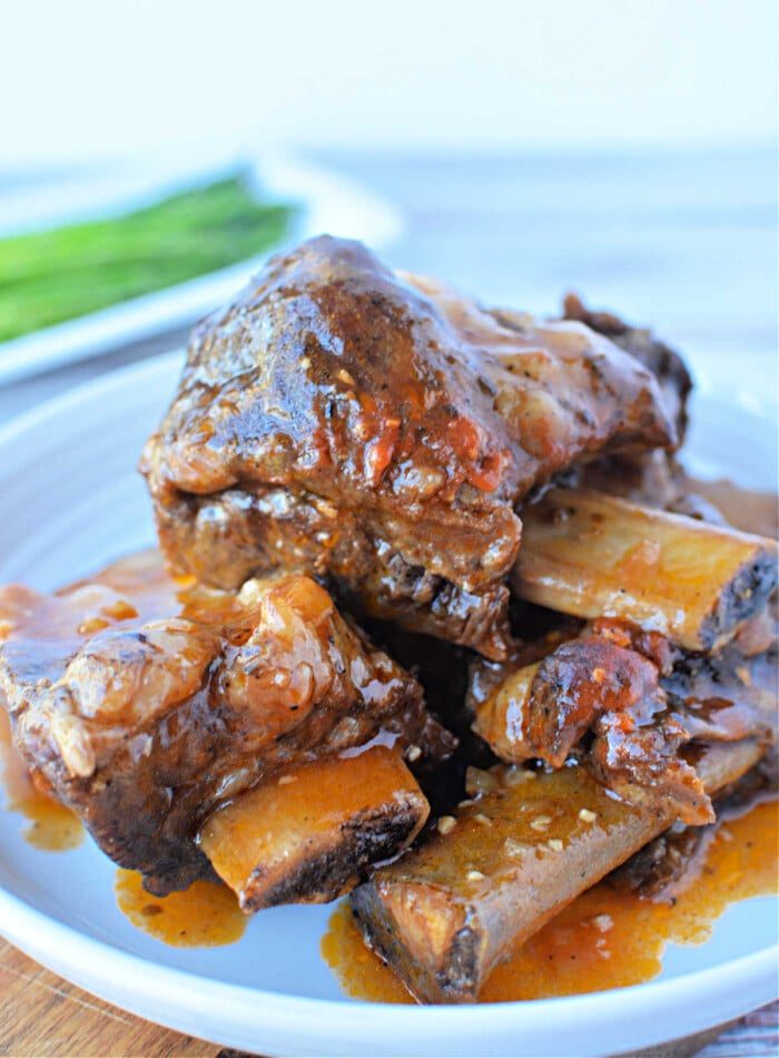 Close-up of a plate featuring mouthwatering braised beef short ribs, simmered to perfection in a pressure cooker and garnished with a rich red sauce, all elegantly presented on a white plate.