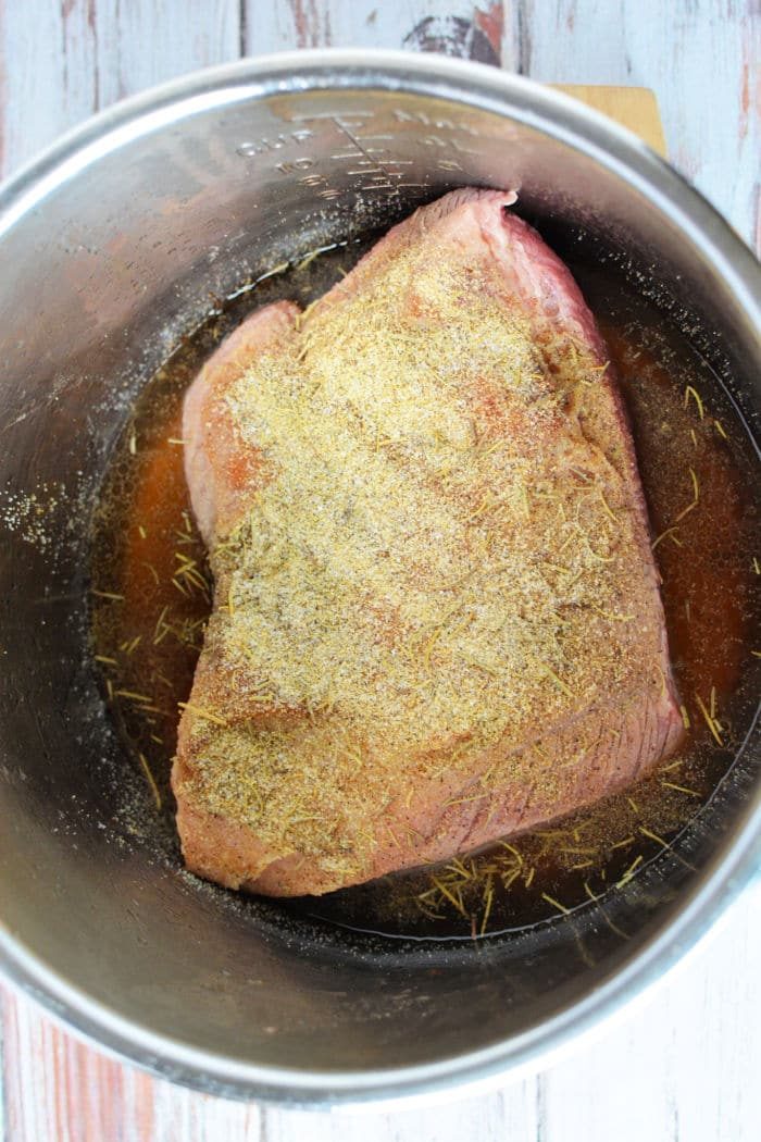 Raw brisket with seasoning sits in a metal pot, ready for transformation into a tender delight, solid for your pressure cooker brisket recipe.