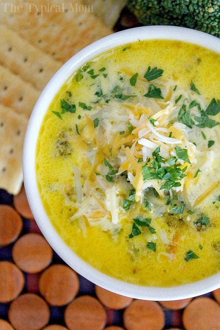 A bowl of Pressure Cooker Broccoli Cheese Soup topped with shredded cheese and parsley, served with crackers.