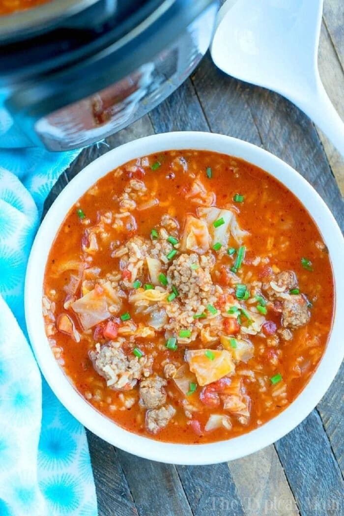 A bowl of hearty pressure cooker cabbage soup with ground beef, rice, and tomatoes sits on a wooden table.