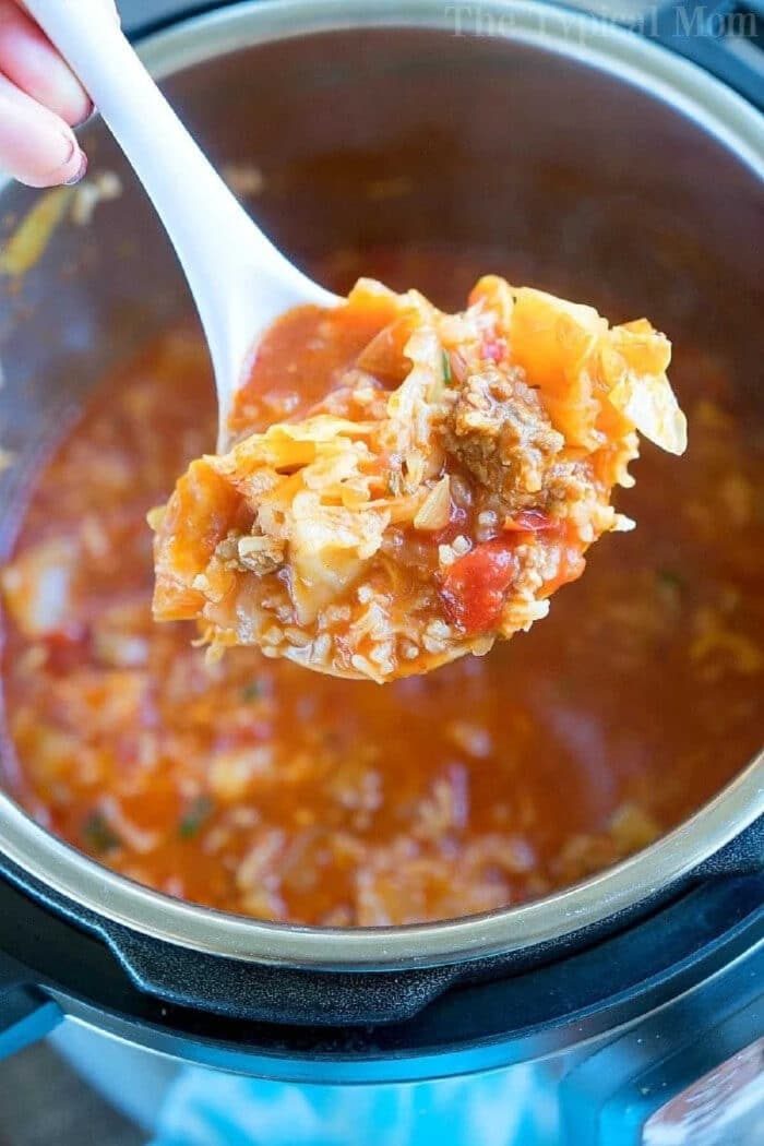 A ladle of hearty pressure cooker cabbage soup with ground meat and tomatoes held over a pot.