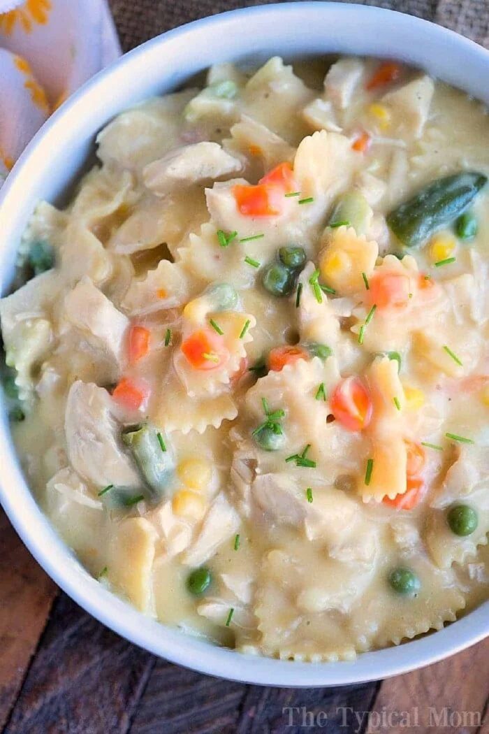 A bowl of creamy chicken noodle casserole with bowtie pasta, vegetables, and herbs on top evokes the comforting essence of a pressure cooker chicken noodle casserole.