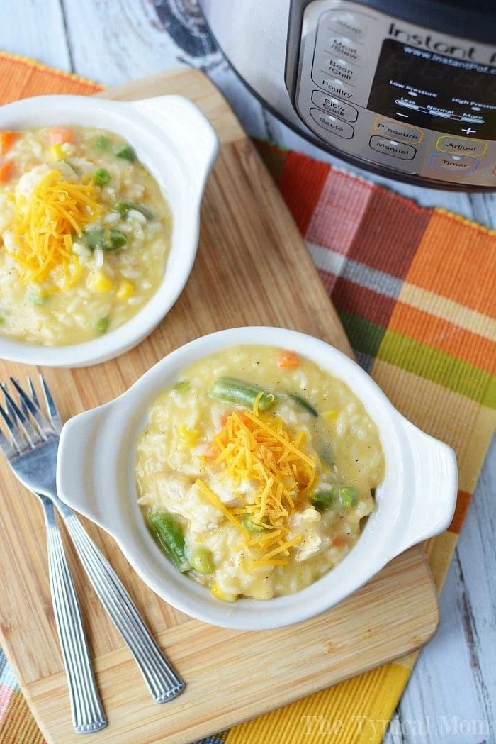 Two white bowls of creamy and tender pieces of pressure cooker chicken and rice sit on a wooden board near an Instant Pot.