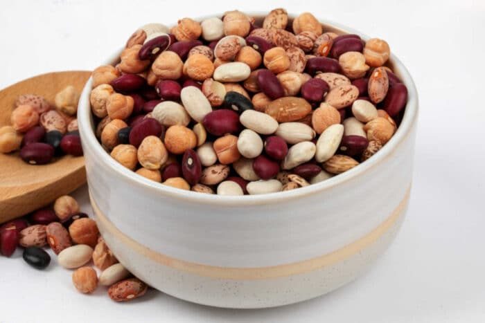 A white bowl filled with assorted dried beans, solid for making pressure cooker chili with dry beans, with more beans scattered in a wooden dish nearby.