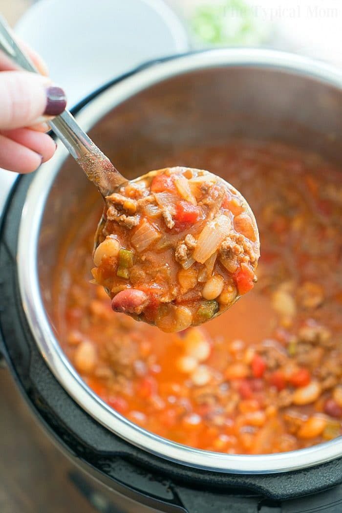 A ladle of chunky chili with beans and vegetables served over a hearty pot of pressure cooker chili with dry beans.