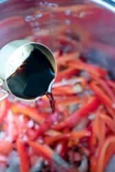 Soy sauce cascades from the measuring cup, enveloping the sliced red peppers in the pressure cooker to create a flavorful Chinese pepper steak.