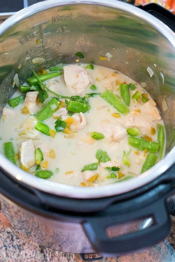 Coconut chicken, green beans, and herbs simmer in a creamy sauce inside an open Instant Pot on a kitchen counter.