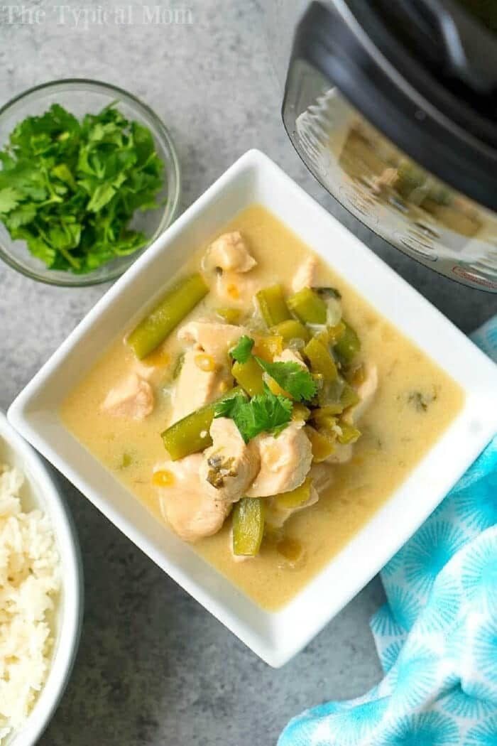 Square bowl of creamy coconut chicken curry with green beans, next to rice, cilantro, and an Instant Pot.