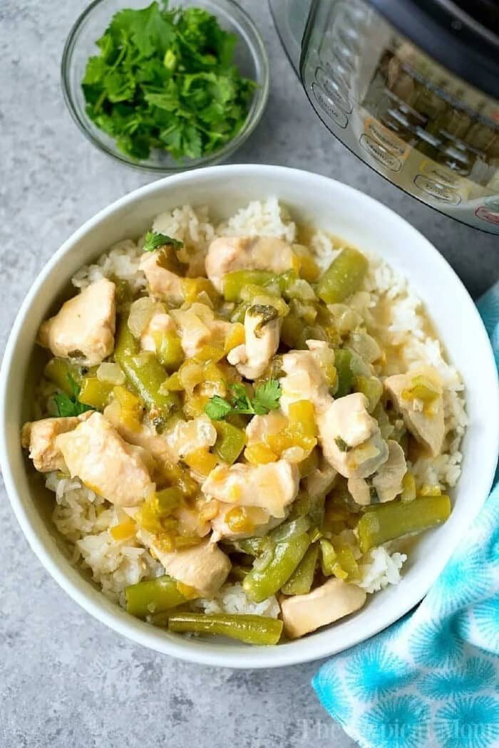 A bowl of rice topped with coconut chicken and green chile stew, garnished with cilantro, with an Instant Pot in the background.