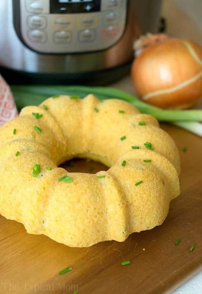 Bundt-shaped pressure cooker cornbread topped with chopped chives on a cutting board, with an onion and Instant Pot behind.