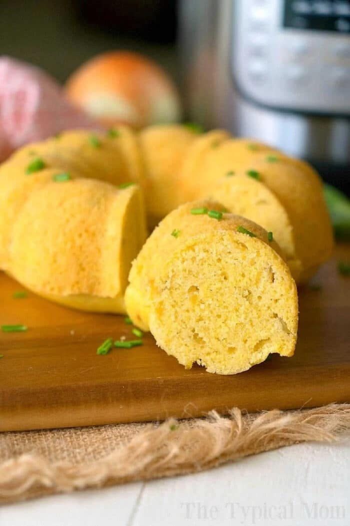 A sliced pressure cooker cornbread ring garnished with chopped chives rests on a wooden board.