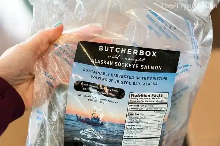 A hand holds a package of ButcherBox wild-caught Alaskan sockeye salmon, solid for pressure cooker fish recipes. The label highlights sustainable harvesting from Bristol Bay, Alaska, with nutrition facts visible on the right side.