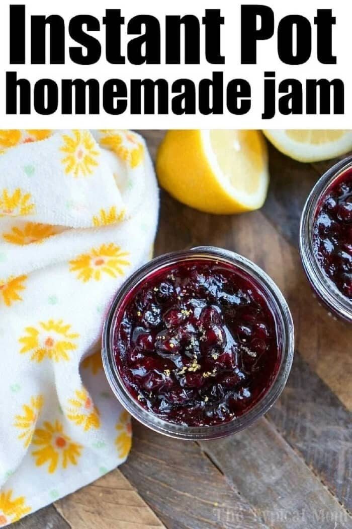 Two jars of homemade pressure cooker jam rest on a wooden surface, accompanied by a cut lemon and a floral towel.