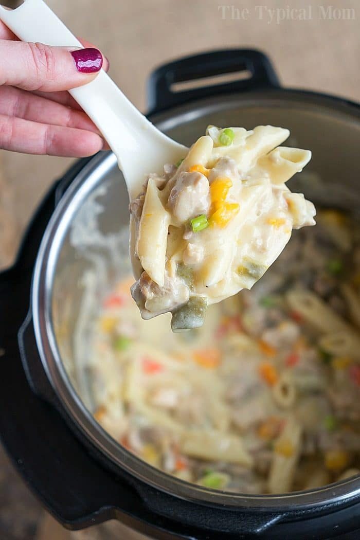 A spoonful of creamy pasta with vegetables and tender chicken, from a good pressure cooker lemon chicken casserole, held over a pot.