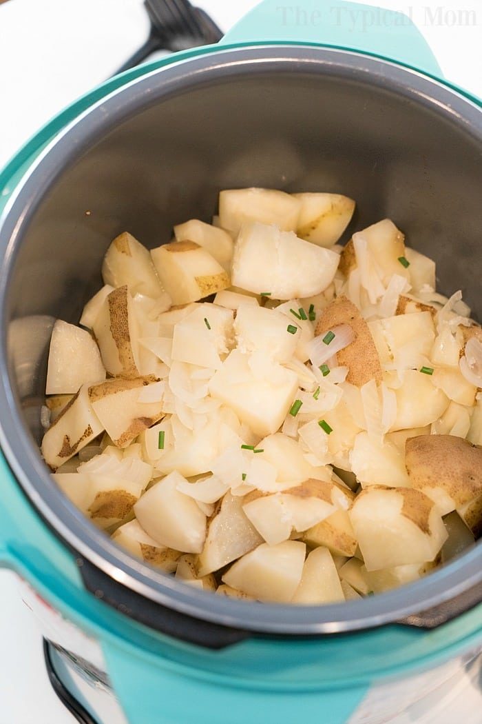 Chopped potatoes and onions gently cook in the teal slow cooker, creating a comforting aroma reminiscent of pressure cooker mashed potatoes.