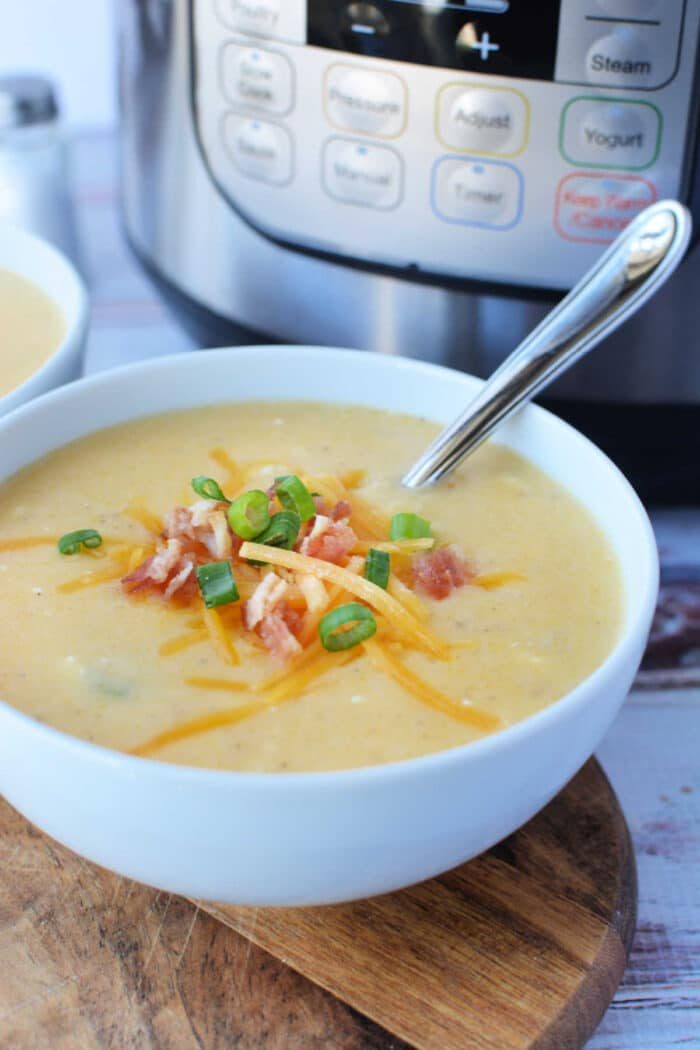 A bowl of creamy potato soup topped with cheese, crispy bacon, and green onions sits invitingly with a spoon beside it, fresh from the pressure cooker.