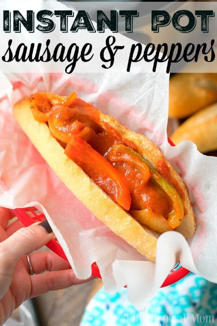 A pressure cooker sausage and peppers sandwich in a red basket lined with white paper, held by a hand.