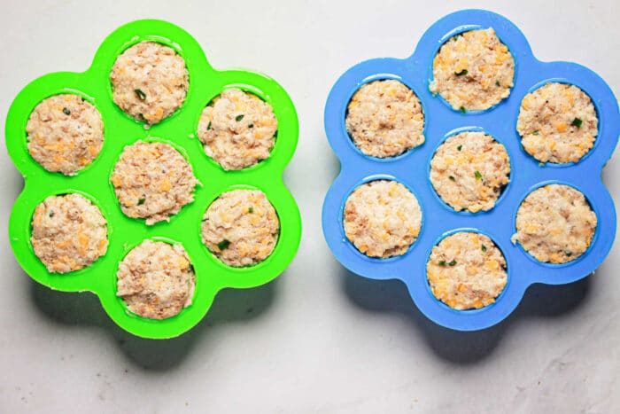 Two silicone molds filled with uncooked sausage balls, one green and one blue, sit on a light gray surface, ready to become good pressure cooker creations.