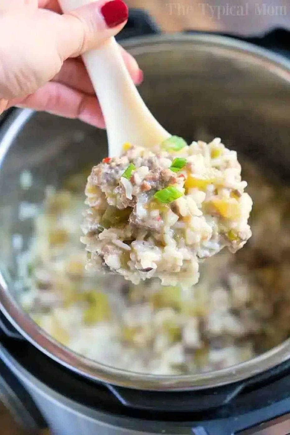 A spoonful of creamy instant pot sausage rice casserole is held over an Instant Pot, topped with chopped green onions.