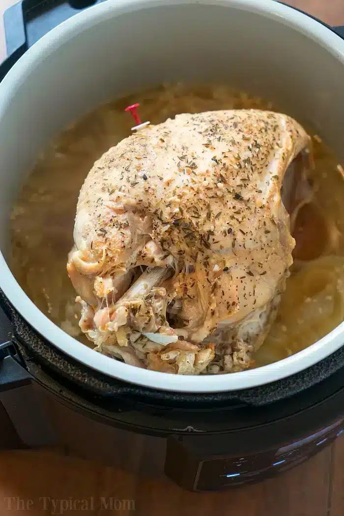 Pressure cooker turkey breast simmers in an ninja foodi, perfectly seasoned with herbs and surrounded by savory broth.