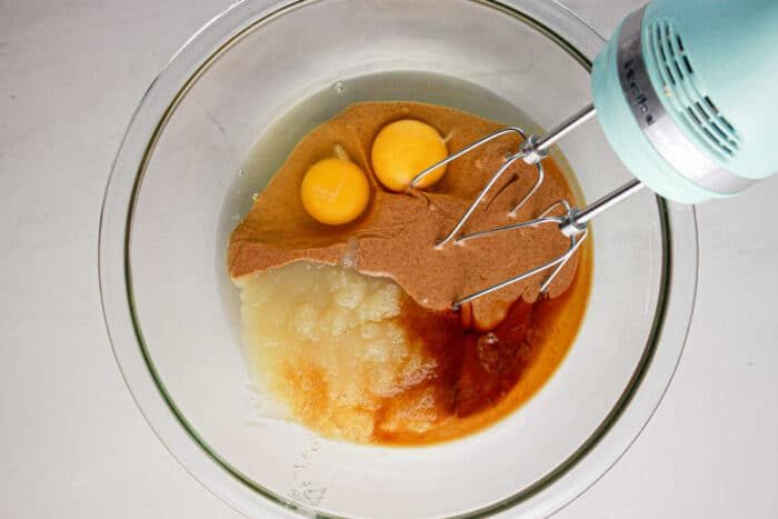 Mixer over a glass bowl with eggs, apple sauce, and batter ready to be mixed for a good protein brownie recipe.
