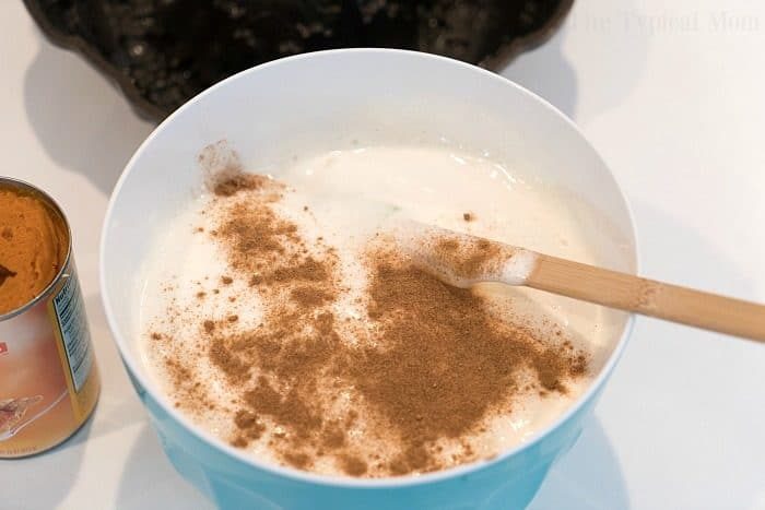 A mixing bowl filled with angel food cake batter and pumpkin spice sits beside a wooden spoon, while a can of pumpkin puree waits to be transformed into a good pumpkin angel food cake.