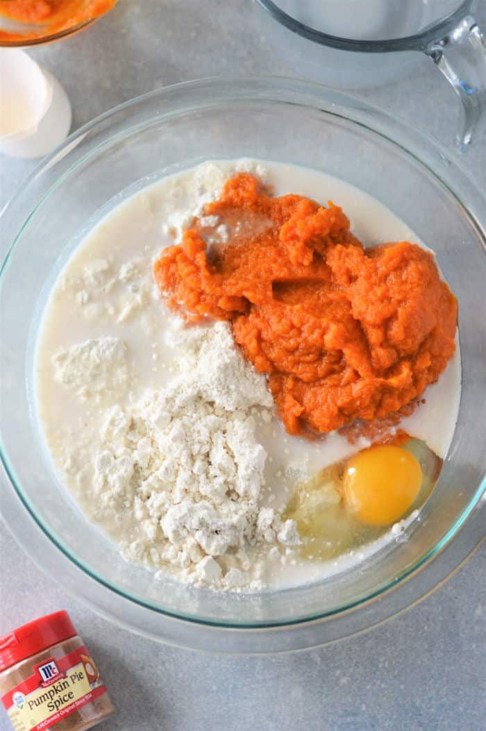 A bowl brims with pumpkin puree, Bisquick, egg, and milk mixture. Nearby, a container of pumpkin pie spice hints at the good transformation into fluffy pumpkin pancakes.