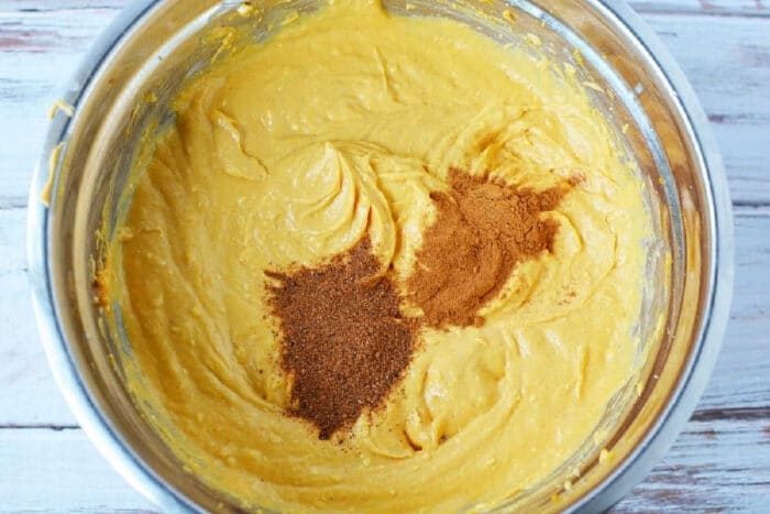 Pumpkin batter in a metal bowl with cinnamon and nutmeg sprinkled on top, ready to be baked into a good sheet pan pumpkin pie.