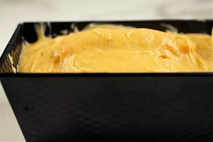 A close-up of thick yellow batter poured into a rectangular black baking pan. The batter appears smooth and fills the pan almost to the top, ready for baking, hinting at the good shape inside the cake to come.