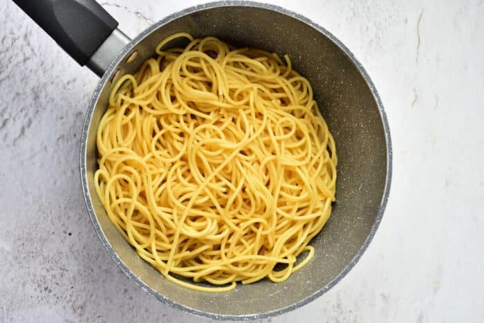 Cooked Pumpkin Spaghetti noodles in a gray pot on a light-colored countertop, viewed from above.